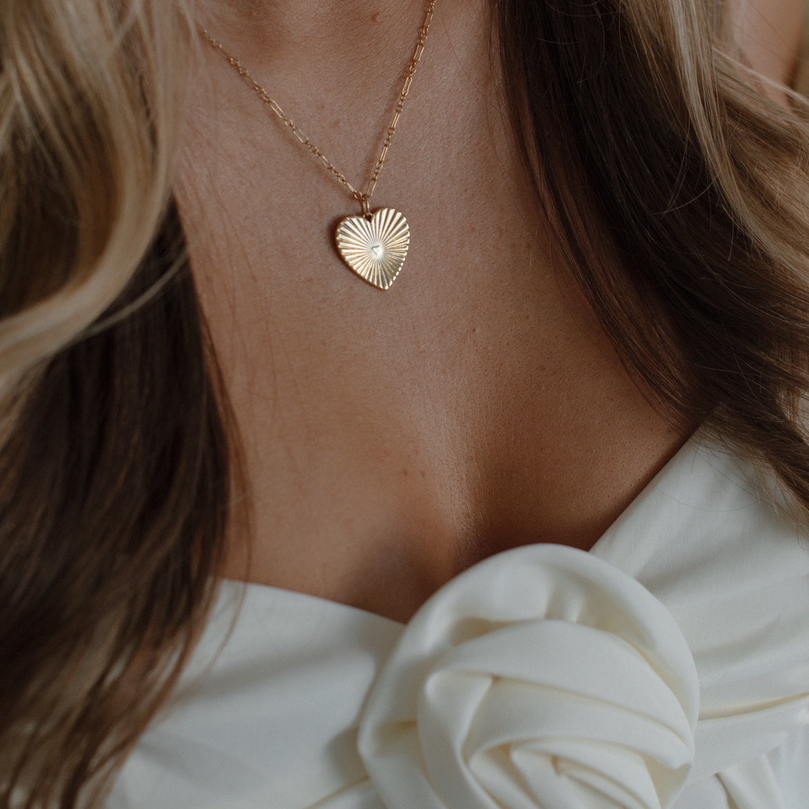 Woman wearing a dainty gold heart necklace layered with everyday jewelry