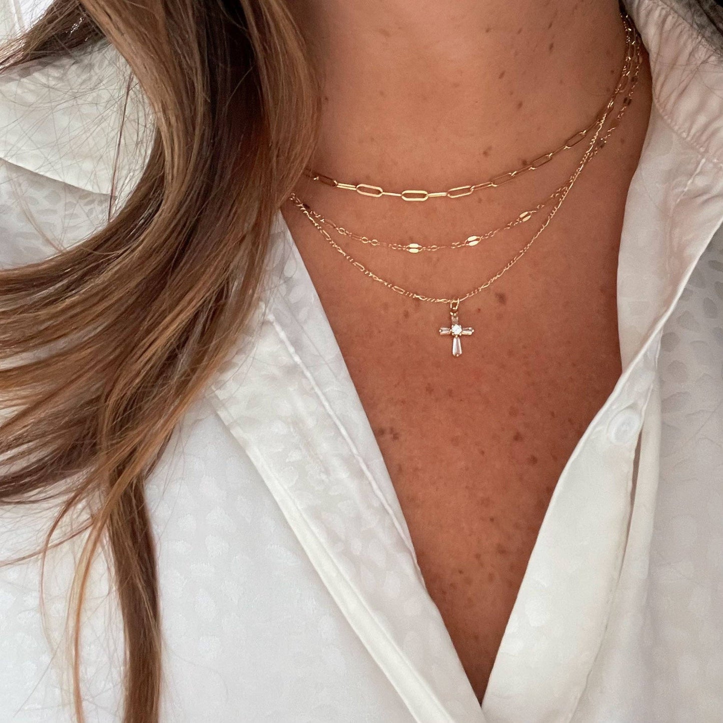 Woman wearing a petite gold cross necklace layered with everyday jewelry