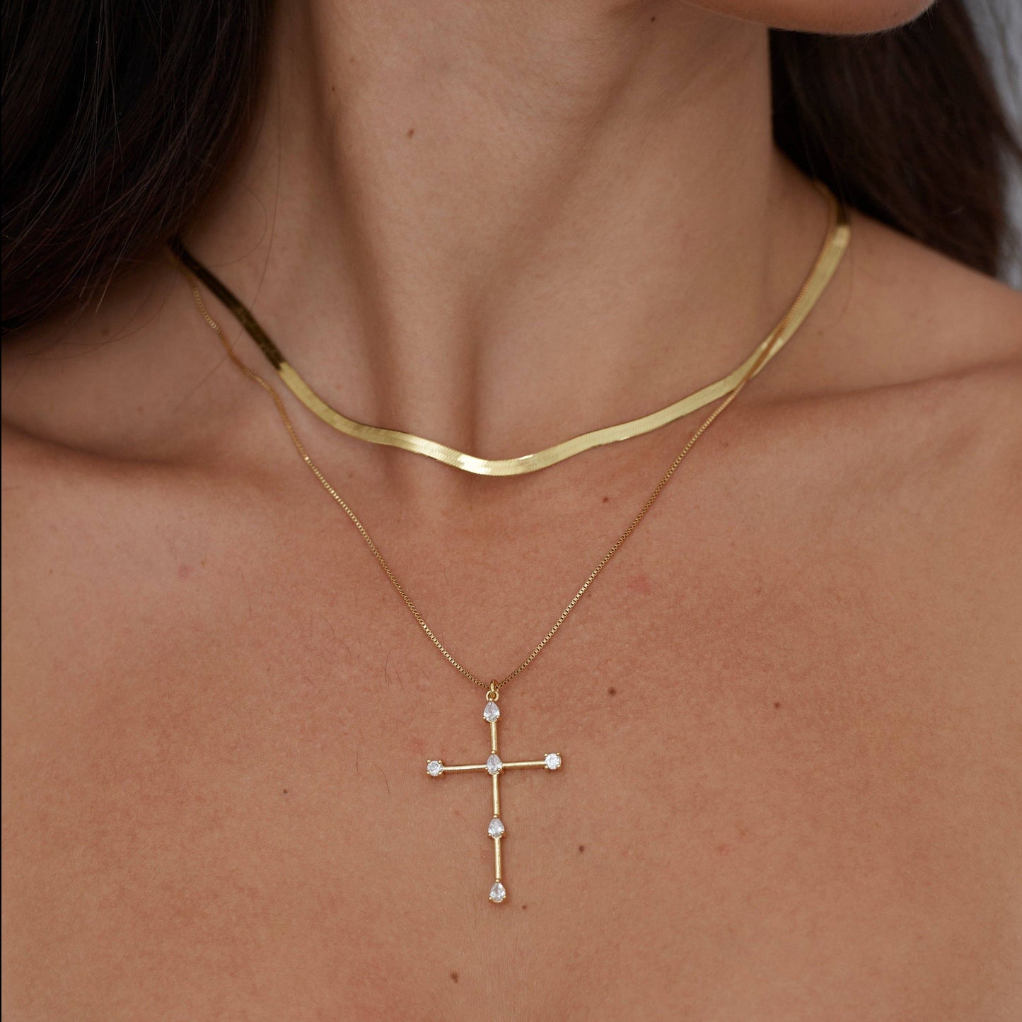 Woman wearing the Tom'e CZ Cross Necklace layered with gold chains