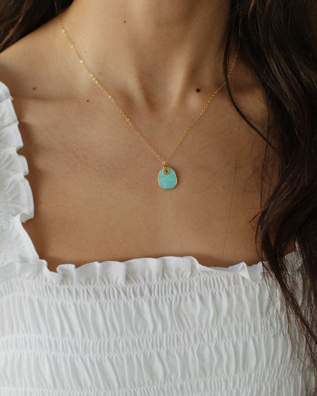 Woman wearing a turquoise pendant necklace layered with dainty gold jewelry